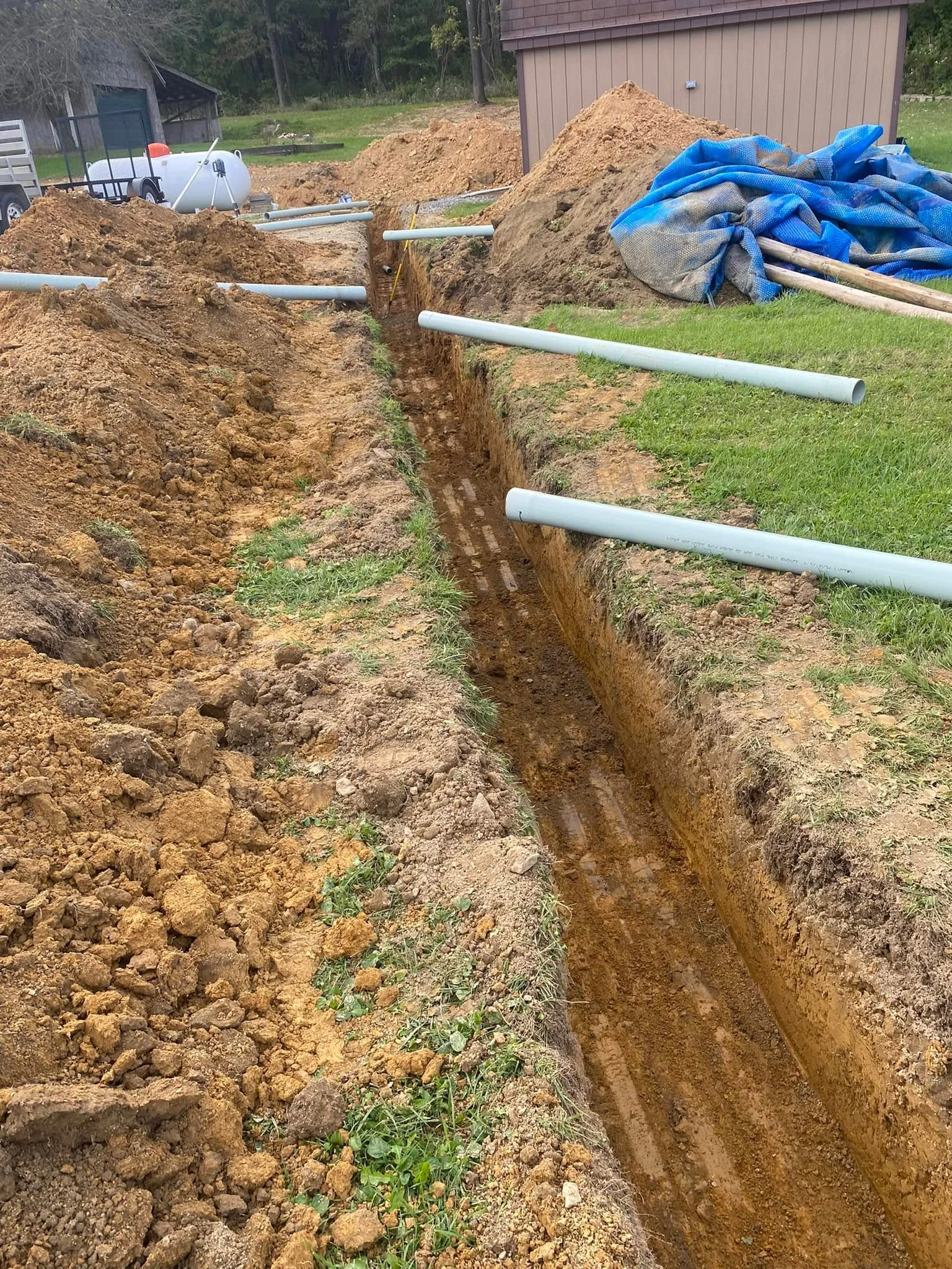Excavated trench with installed PVC drainage pipes and protective mesh covering