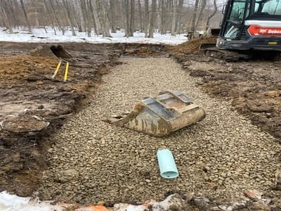 Excavated driveway site with gravel base, removed asphalt, and compact equipment