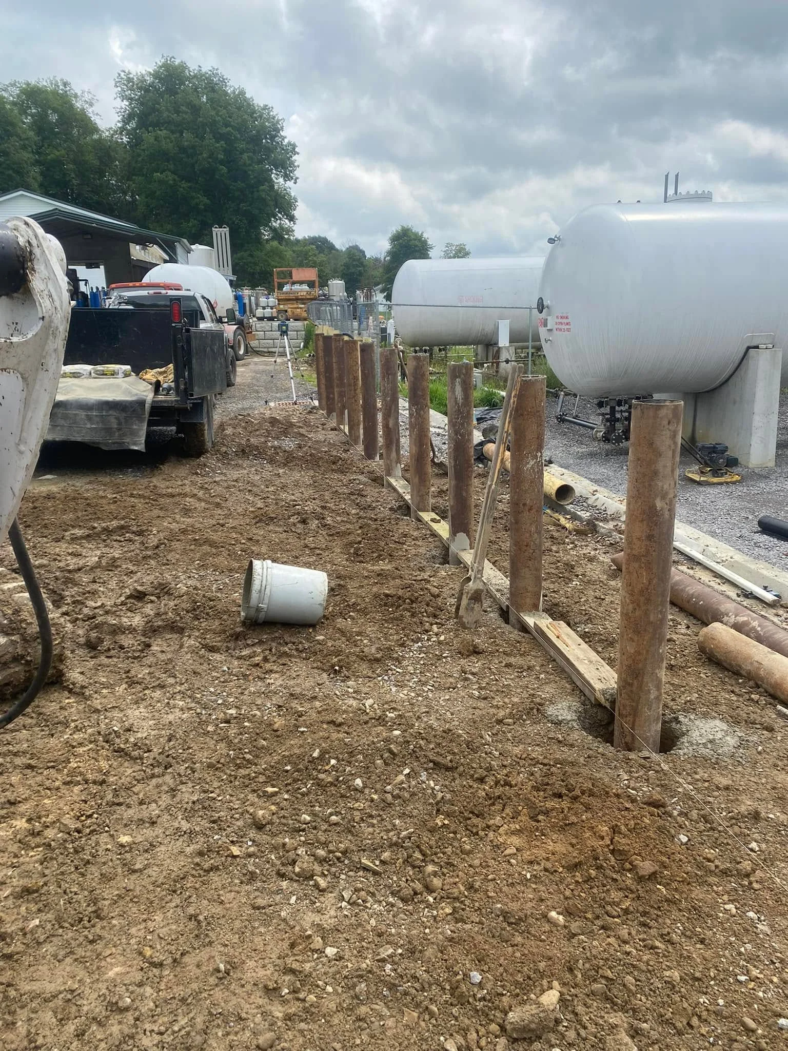 Septic tank installation with metal storage tank, wooden post fence, and gravel base preparation