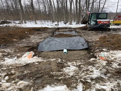 Septic tank installation with excavated basin, geotextile fabric, and heavy equipment on-site