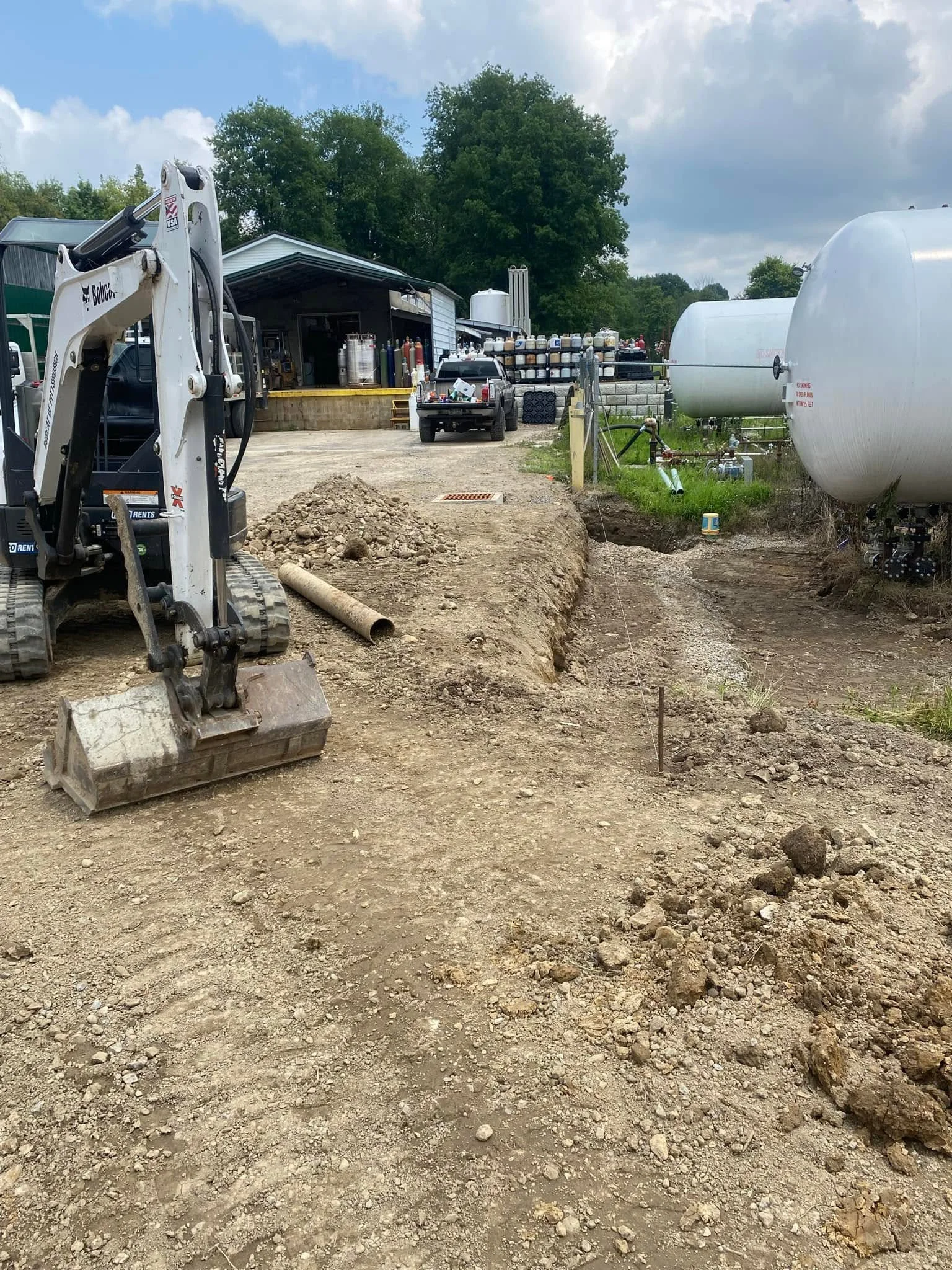 Compact excavator digging septic leach field trench with perforated pipe and gravel base material