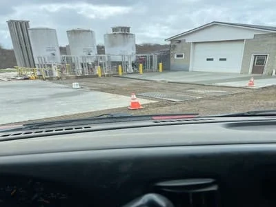 Excavated commercial lot with concrete pad, yellow safety bollards, and industrial storage tanks