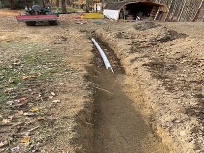 Excavated drainage trench with white PVC pipe installed, sloped earth banks on either side