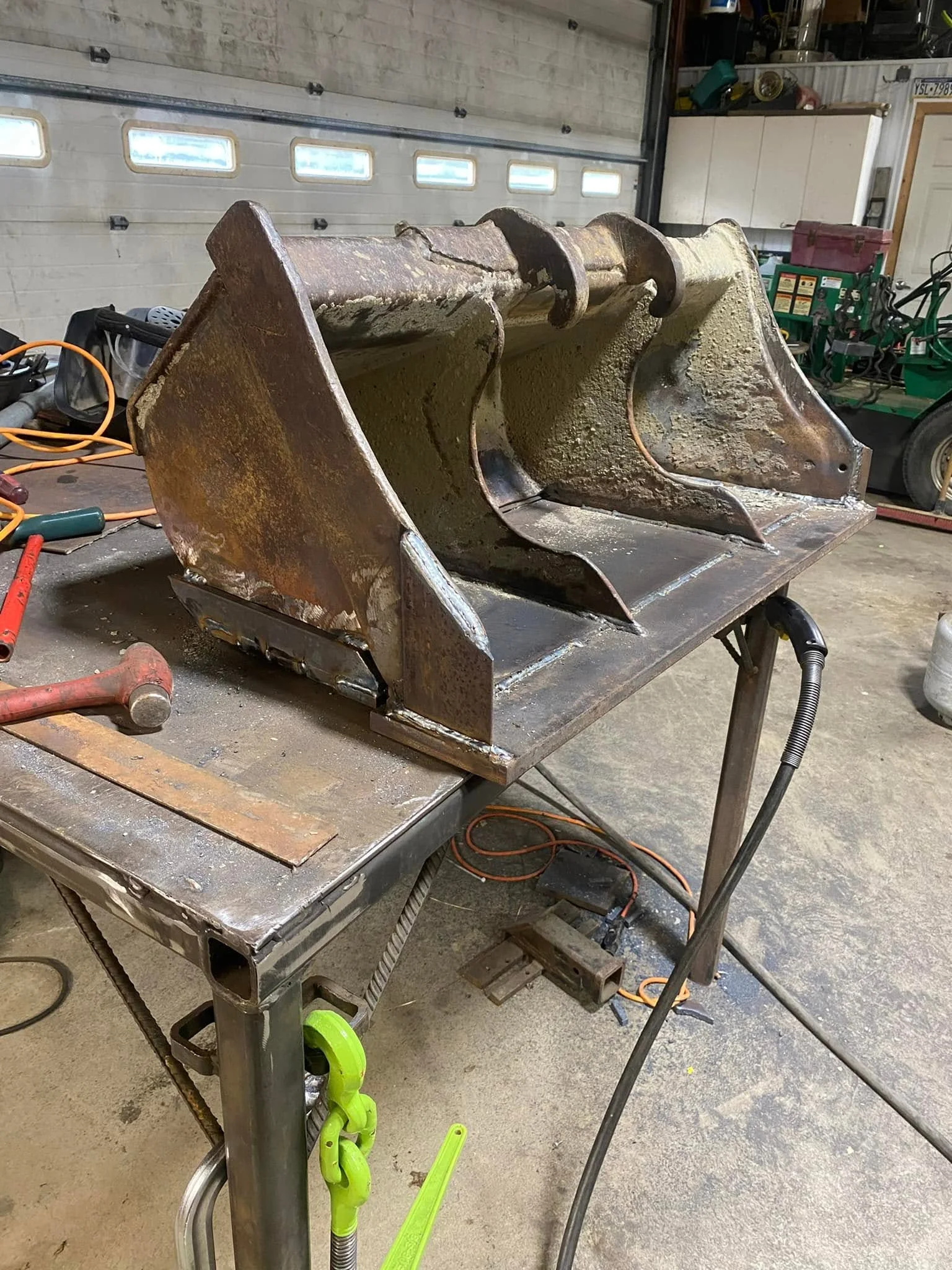 Restored excavator bucket with welded steel reinforcement on work stand in garage