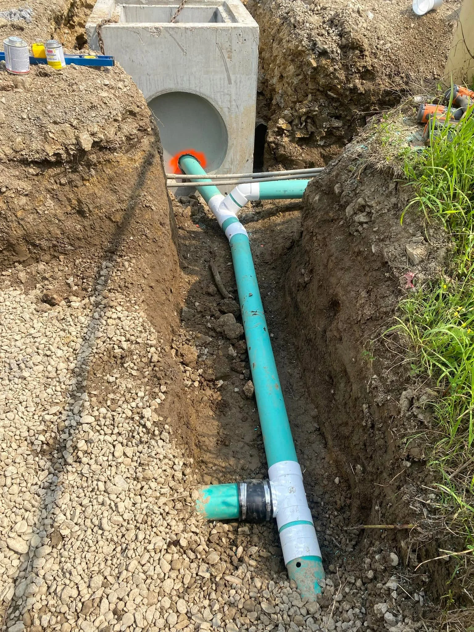 Turquoise PVC drainage pipe connected to precast concrete vault in excavated trench with gravel base
